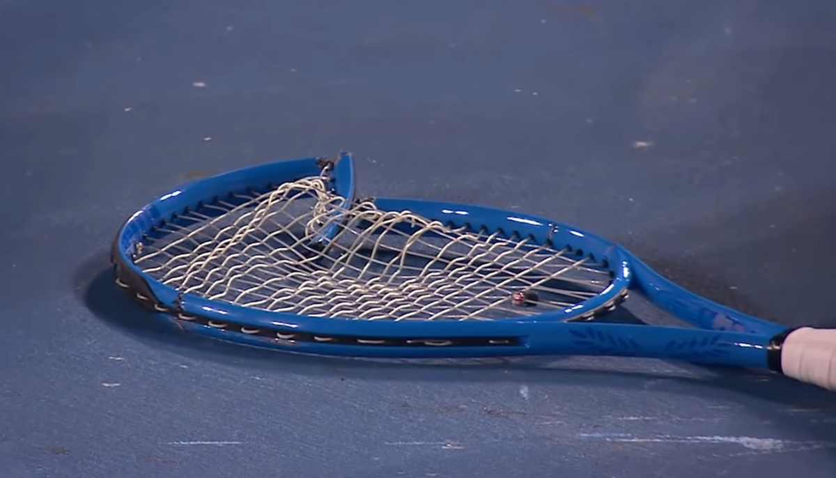 Broken blue tennis racket lying on court